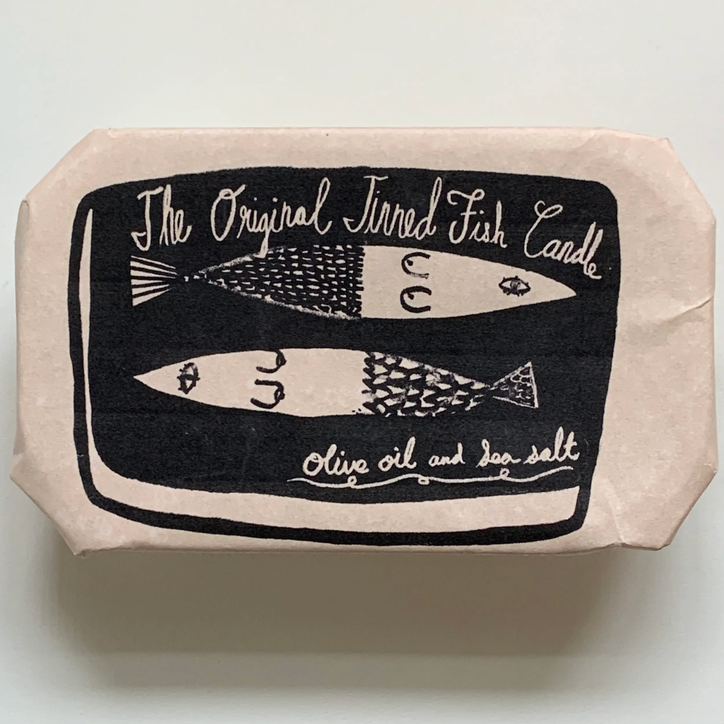 container labeled "tinned fish candle" wrapped in paper with a white background