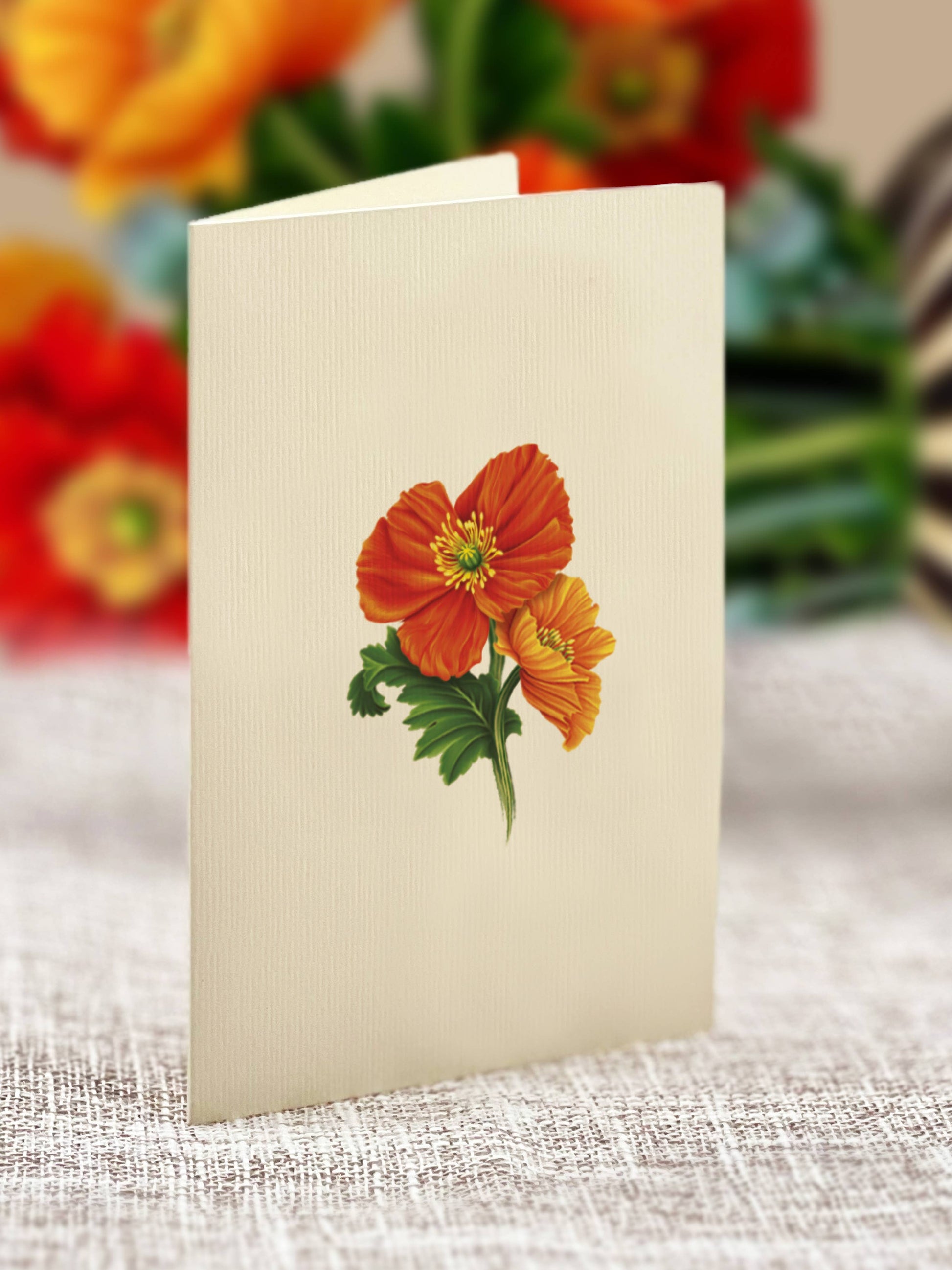 Card with orange flower illustration on a textured surface with blurred flowers in the background