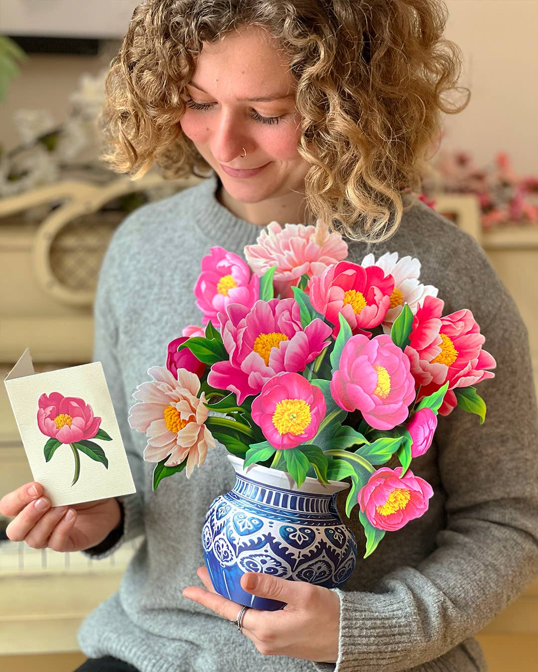 Person holding a bouquet of pink flowers and a card with a floral design.