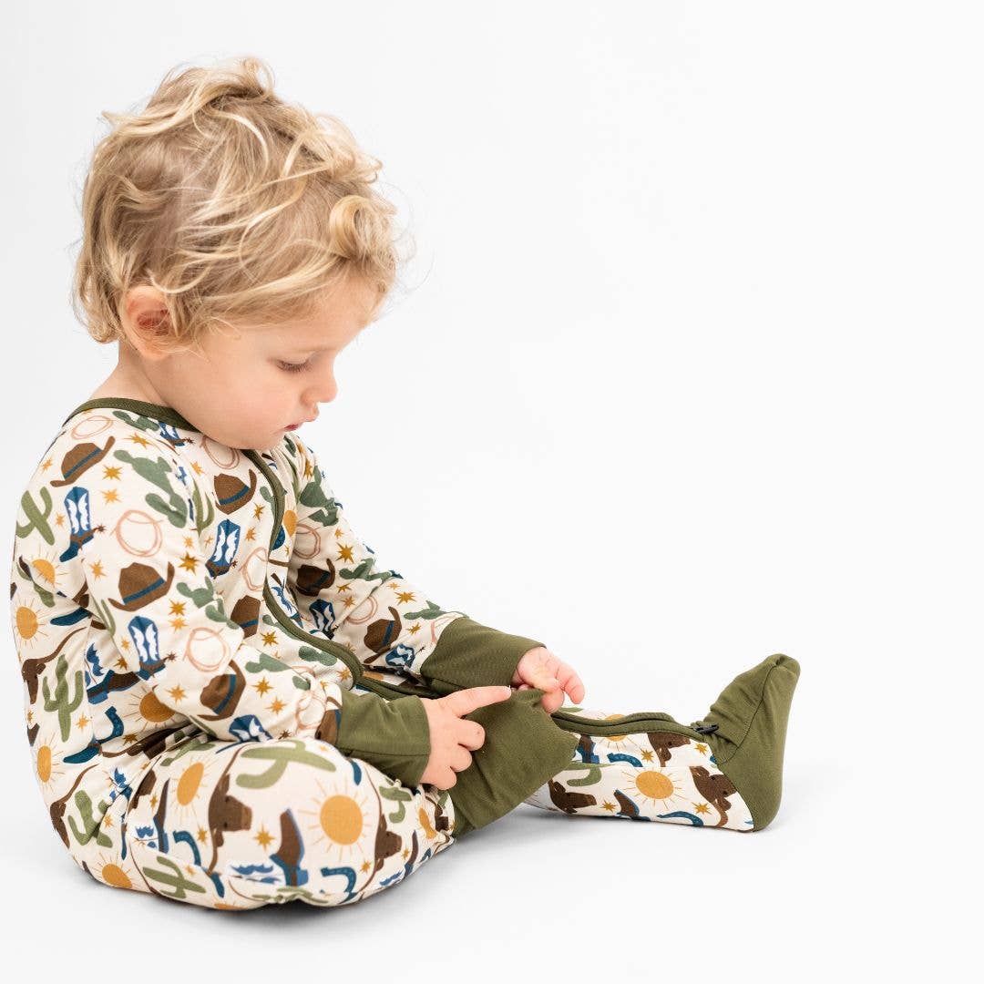 Child wearing a patterned onesie with cowboy design on a white background