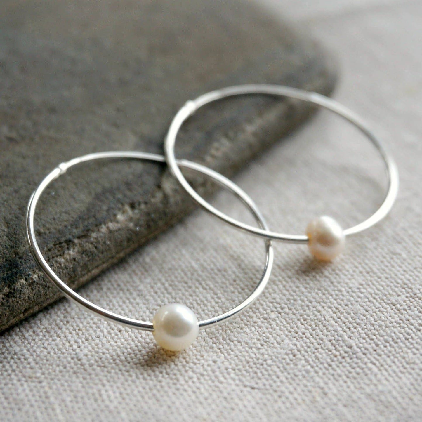 Silver hoop earrings with pearls on a stone and fabric background