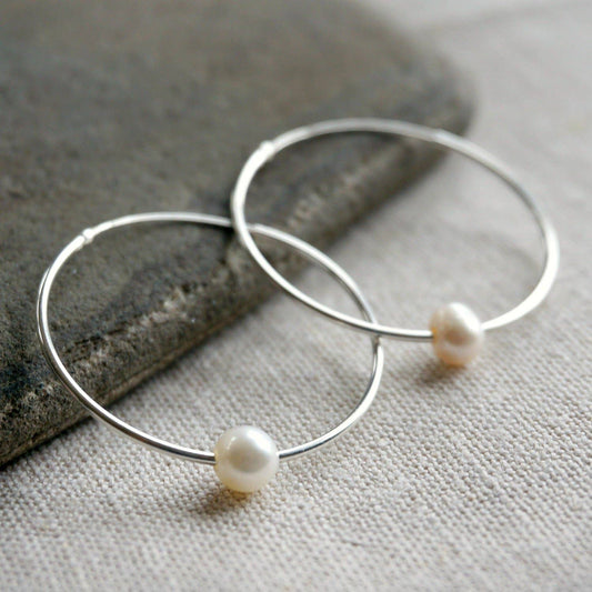 Silver hoop earrings with pearls on a stone and fabric background
