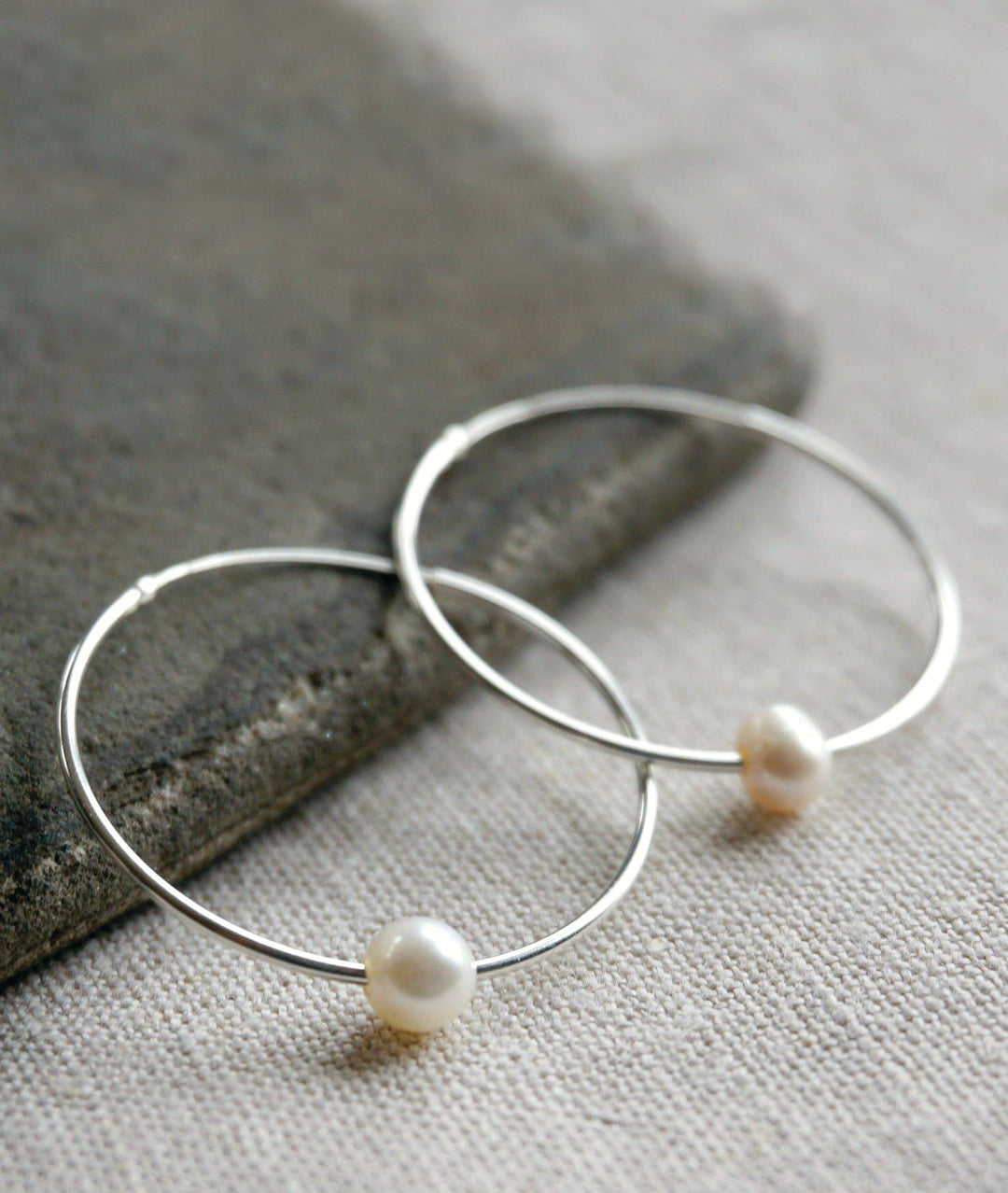 Silver hoop earrings with pearls on a stone and fabric background