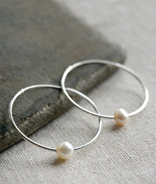 Silver hoop earrings with pearls on a stone and fabric background