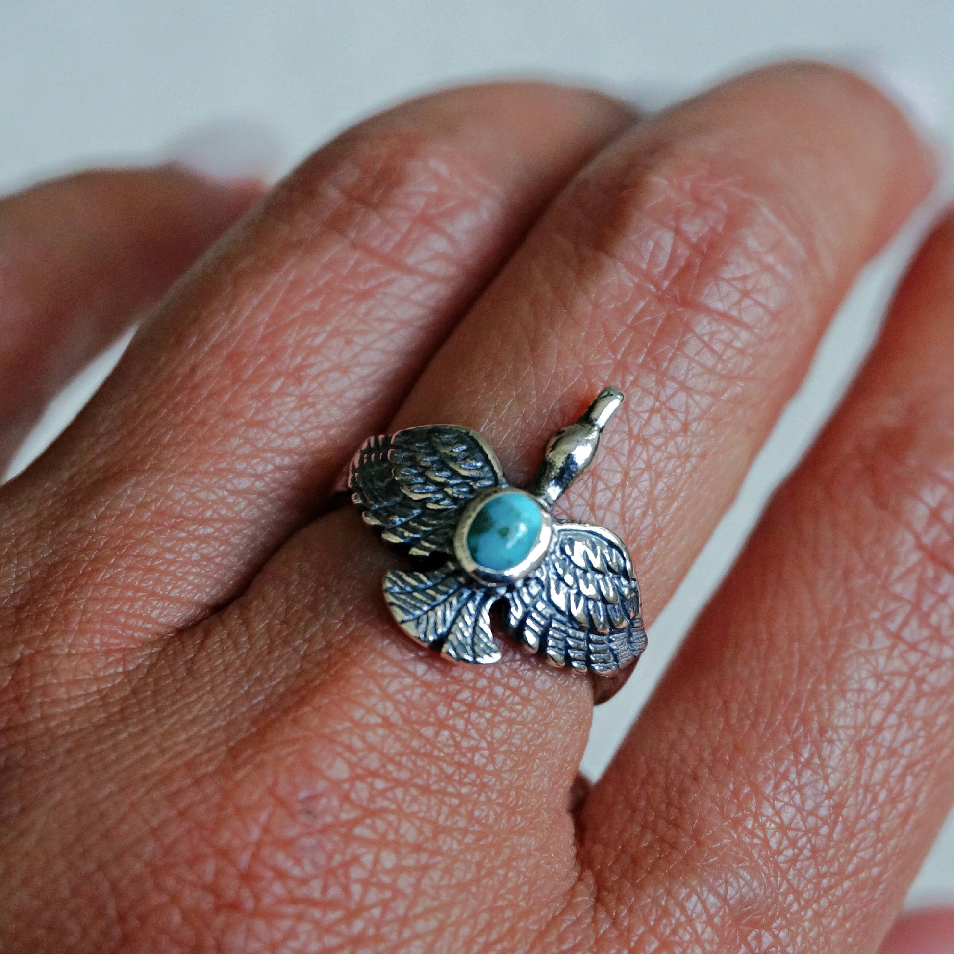 Silver ring with turquoise stone on a finger against a white background