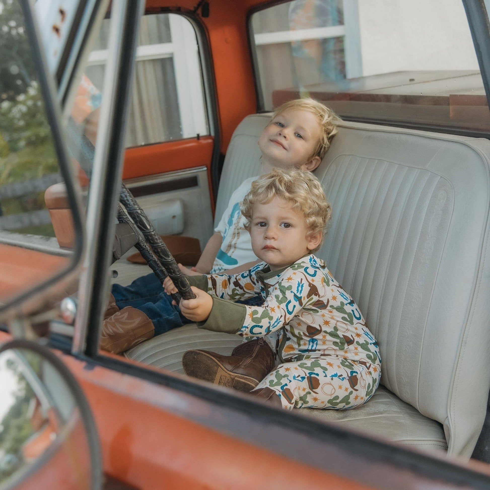 Two children sitting inside an old-fashioned vehicle, with one holding a steering wheel.