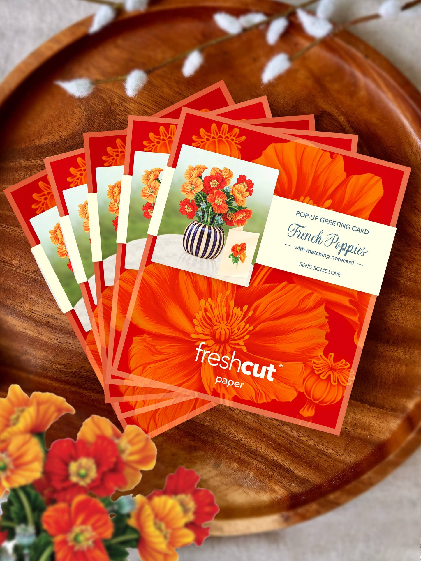 Stack of 'freshcut' paper pop-up greeting cards on a wooden surface with flowers.