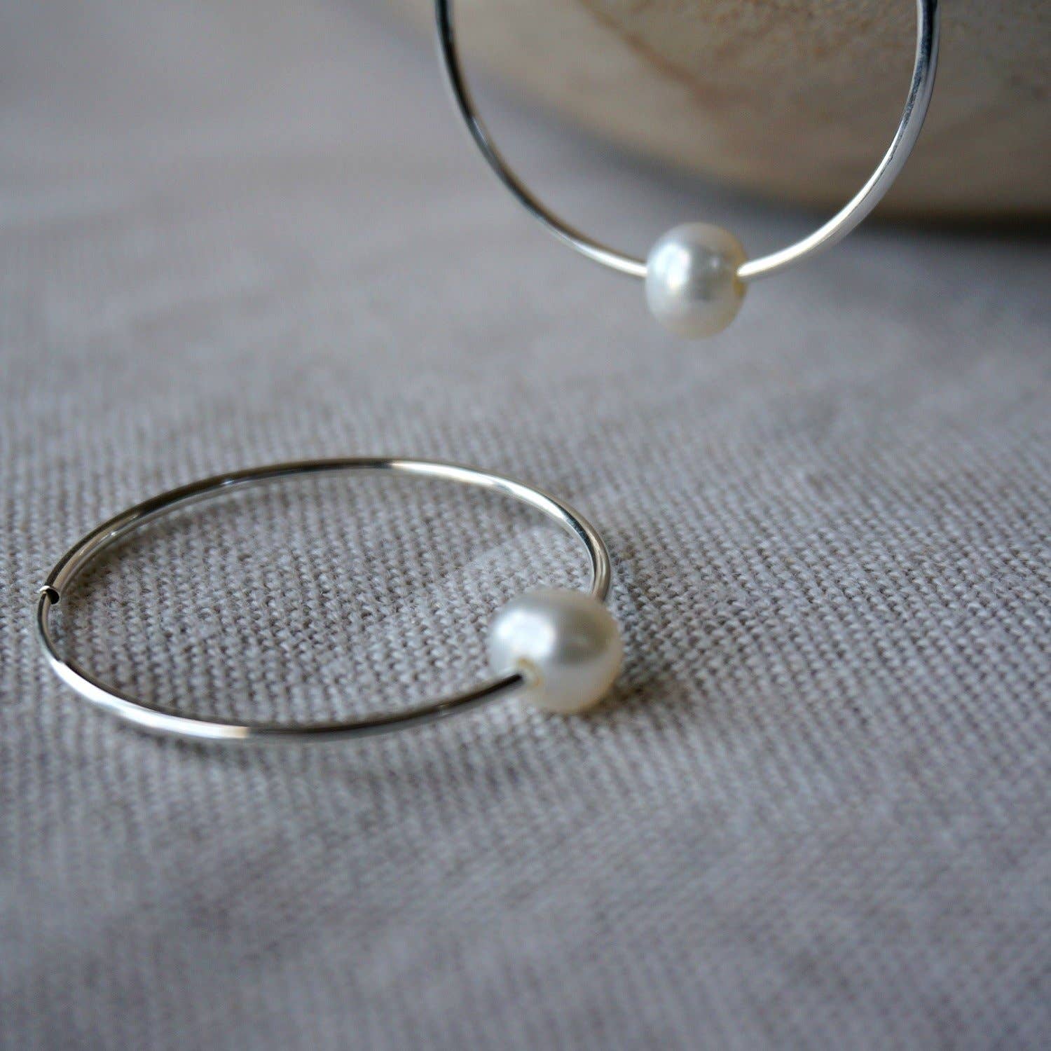 Silver hoop earrings with pearls on a textured fabric background