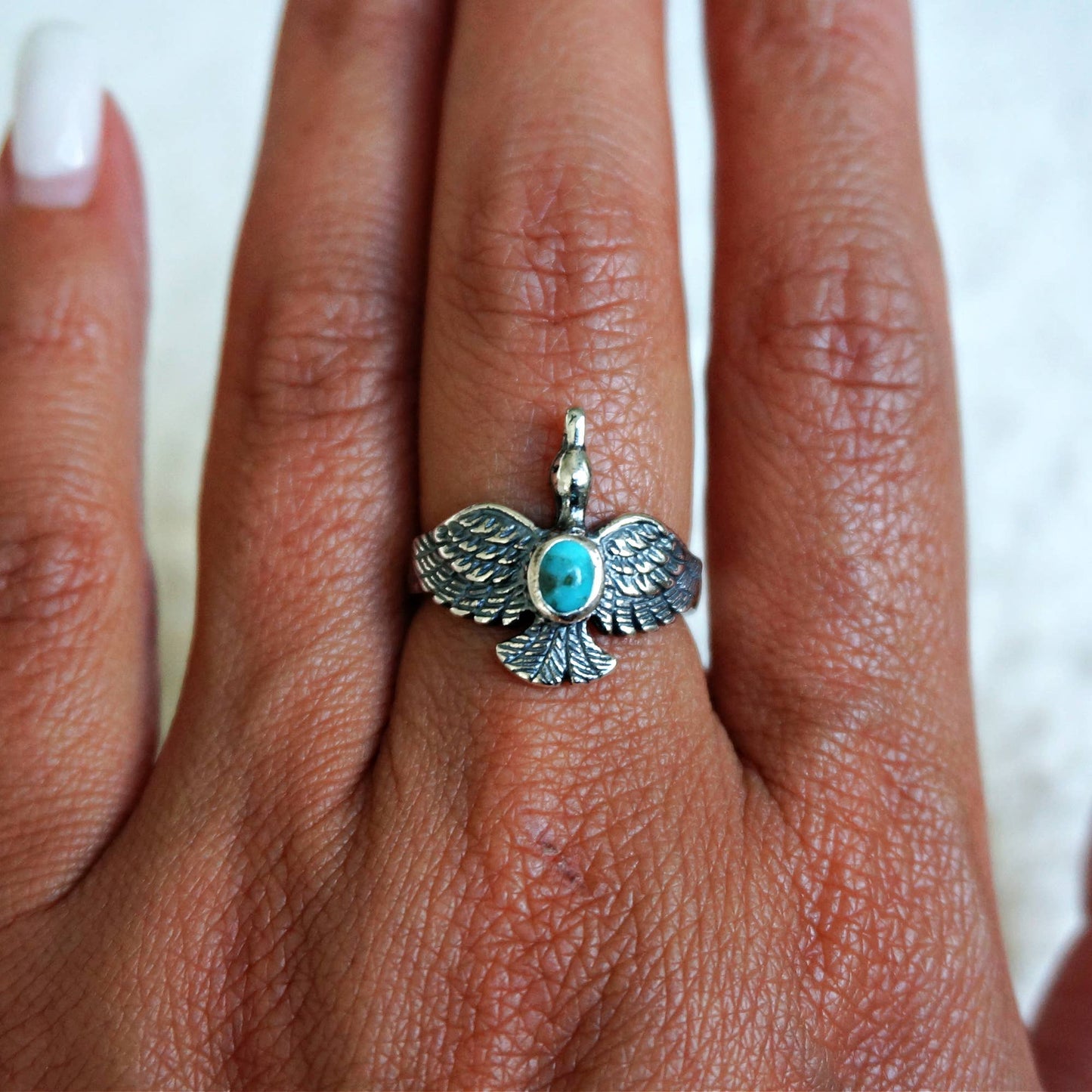 Silver ring with a turquoise stone on a person's finger against a white background