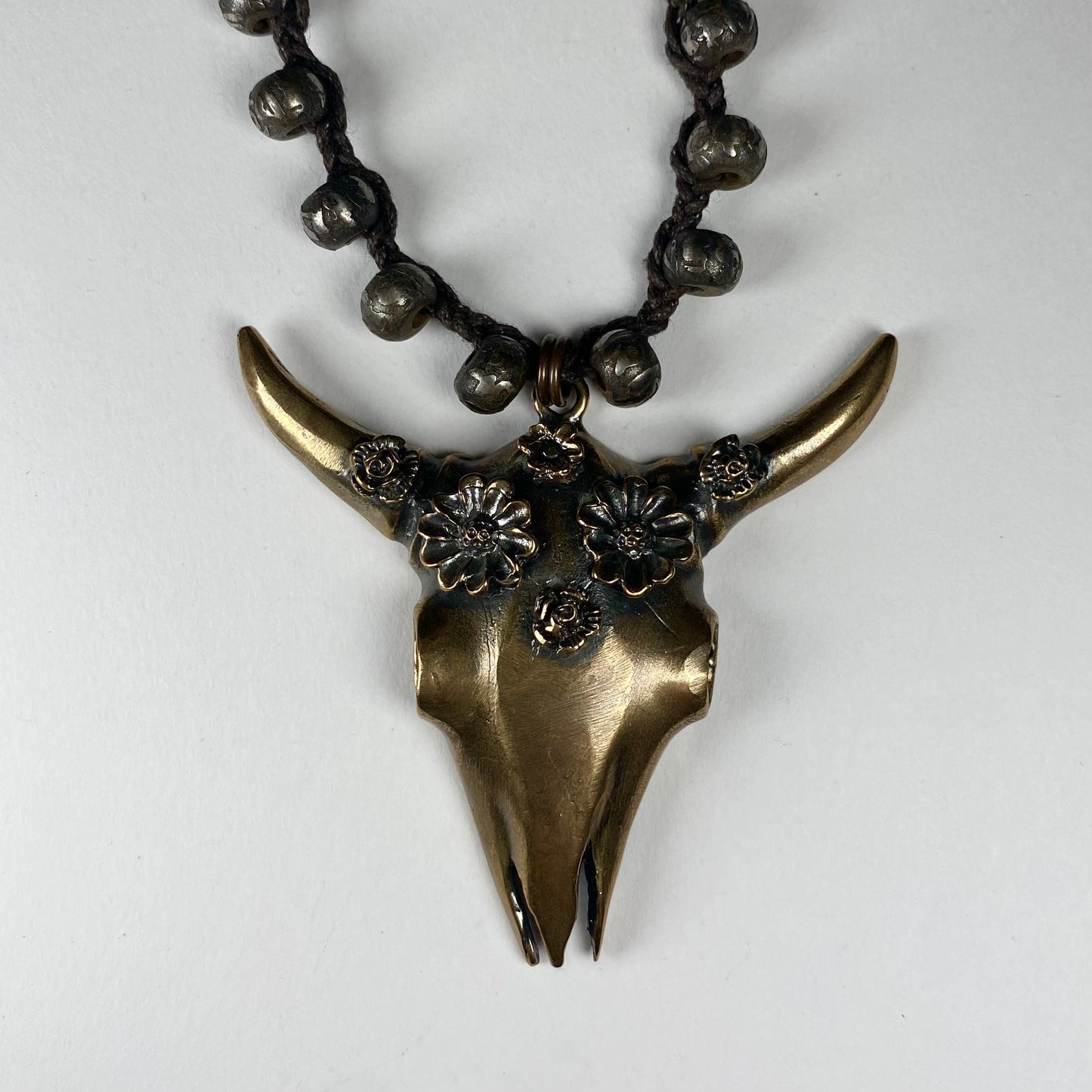 Closeup of Bronze  pendant of a Cattle Skull with flower crown.