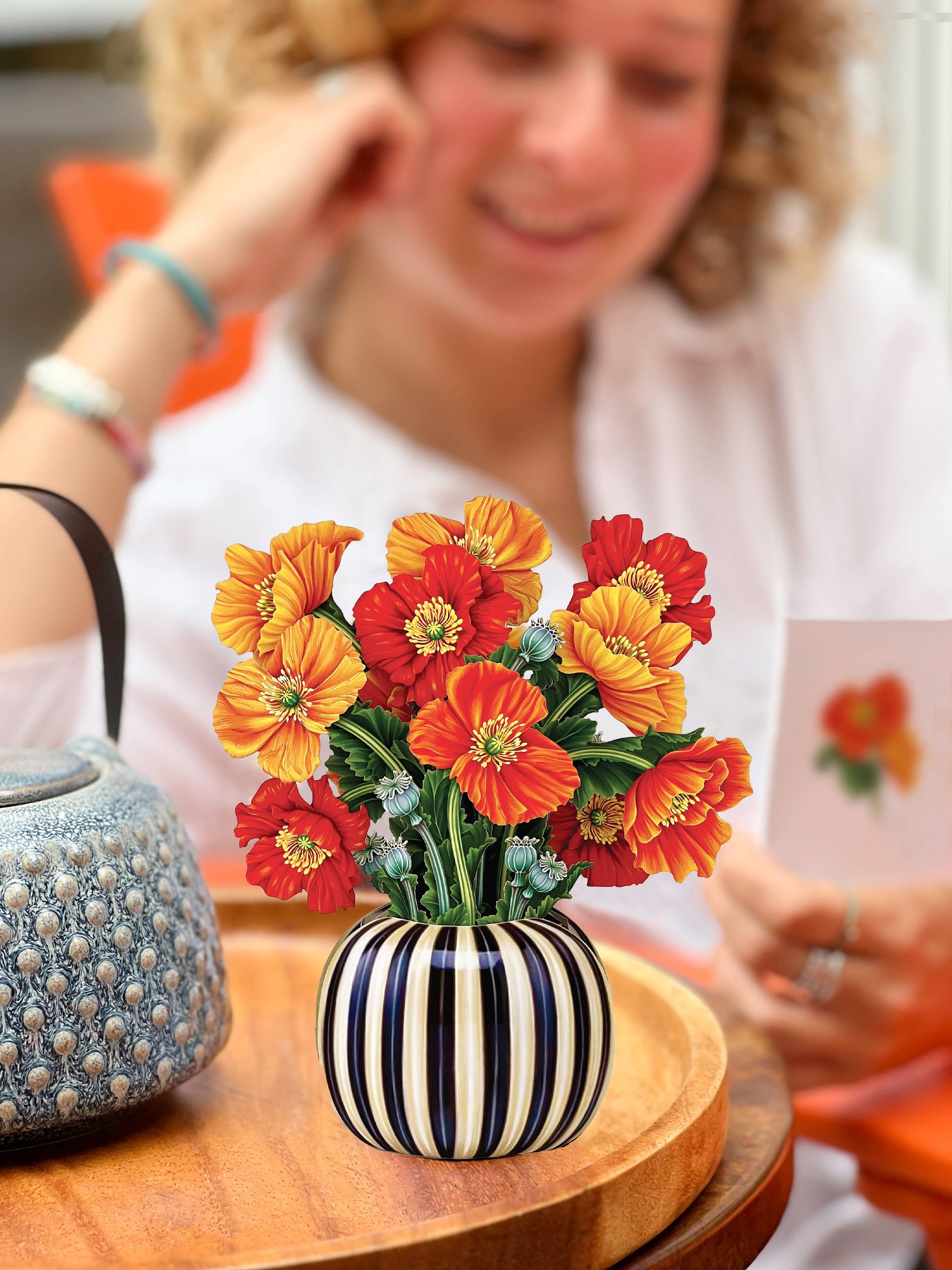 Striped vase with colorful flowers on a wooden table, blurred person in the background