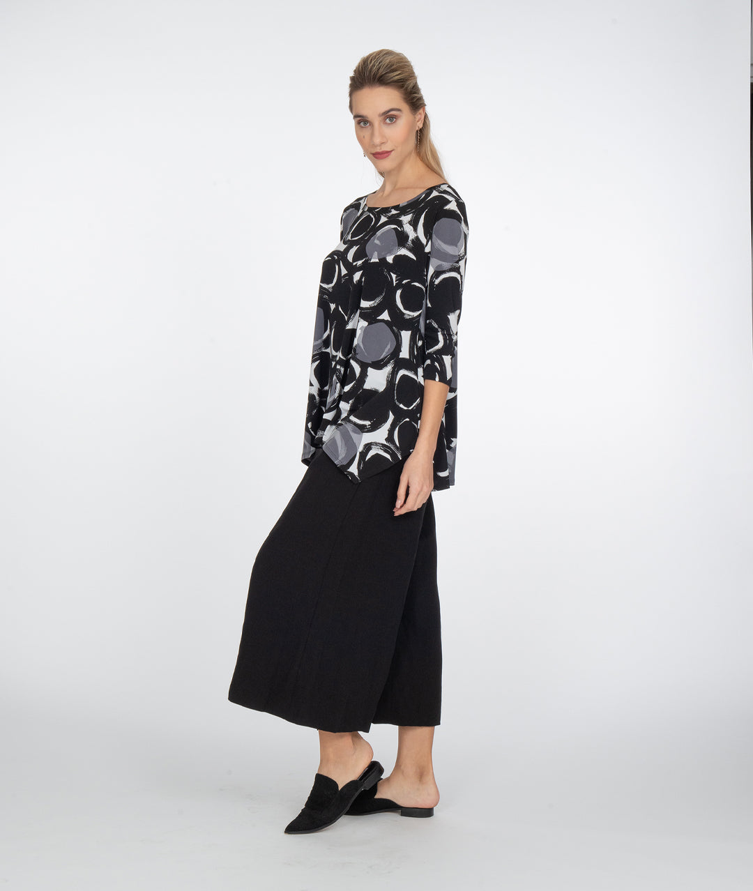 model in a wide leg black pant, with a black, white and grey circle print top with a hankerchief hem