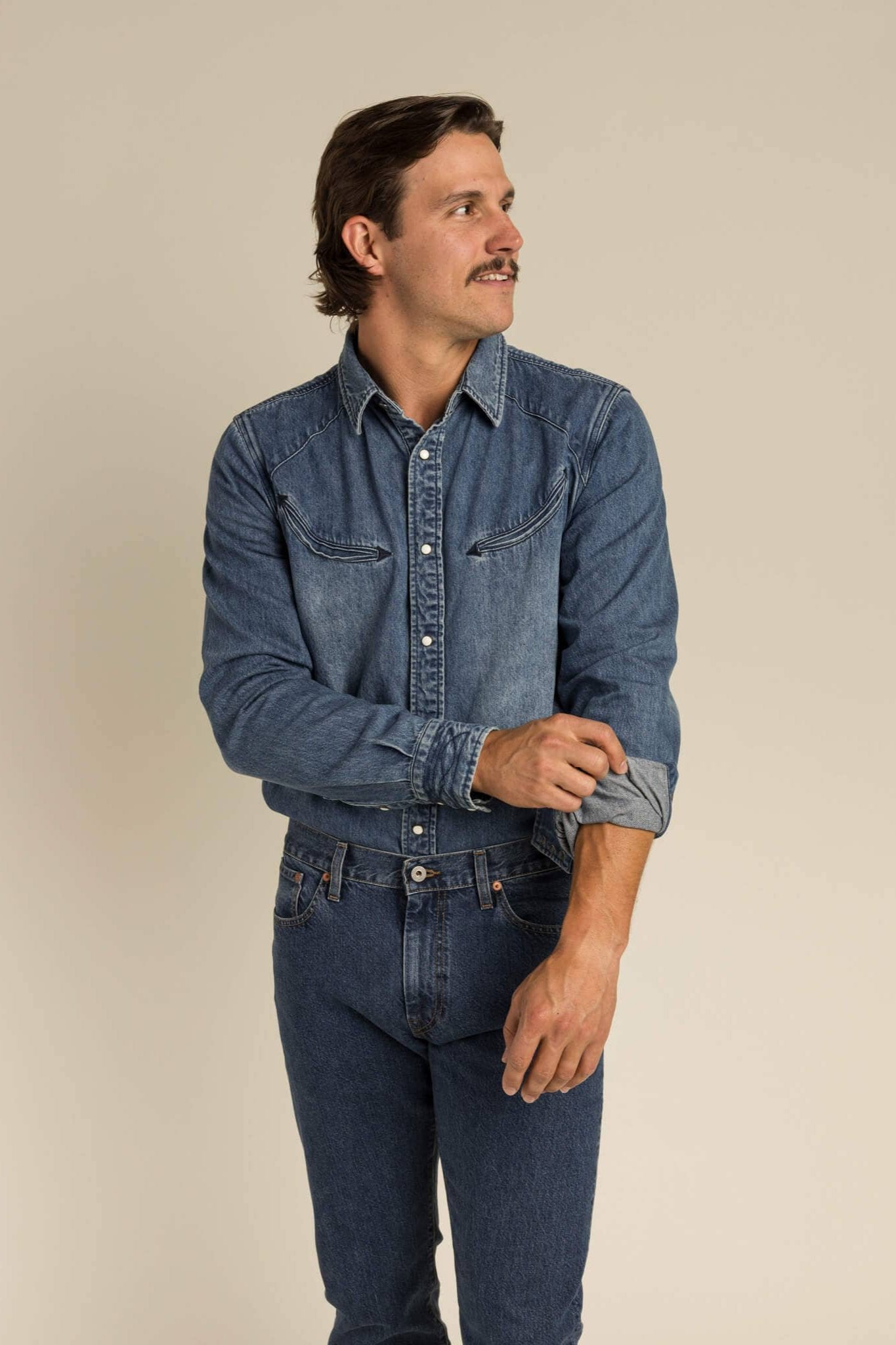 model wearing idigo denim collared long sleeve, with arrow stitching pockets and pearl snaps. paired with jeans.