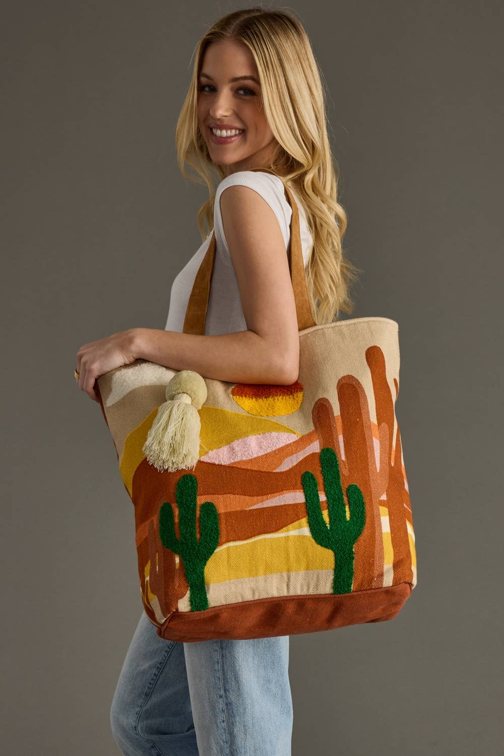 Woman holding a colorful tote bag with desert design against a gray background