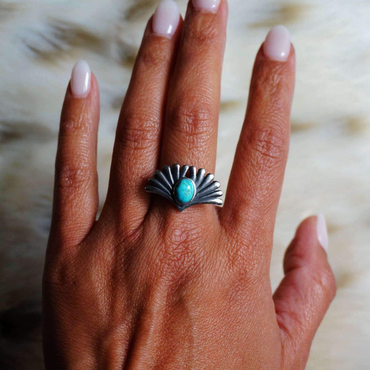 Hand wearing a silver ring with a turquoise stone on a blurred background