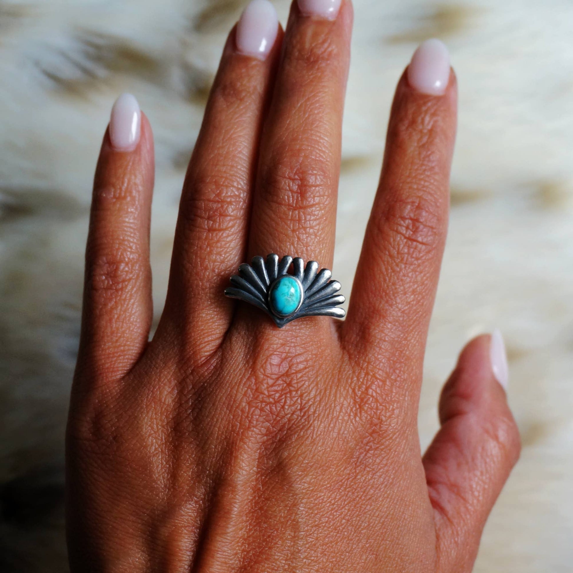 Hand wearing a silver ring with a turquoise stone on a blurred background