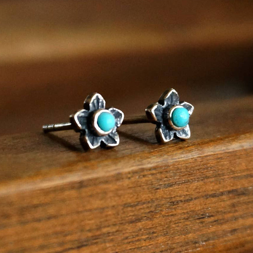 Flower-shaped earrings with turquoise centers on a wooden surface