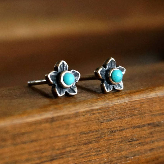 Flower-shaped earrings with turquoise centers on a wooden surface