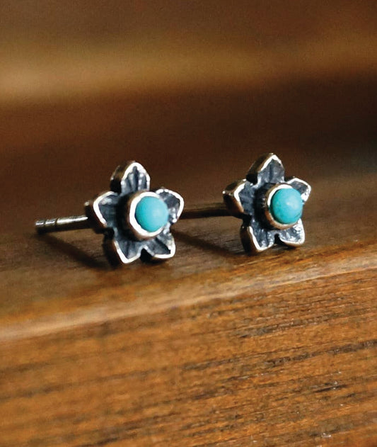 Flower-shaped earrings with turquoise centers on a wooden surface