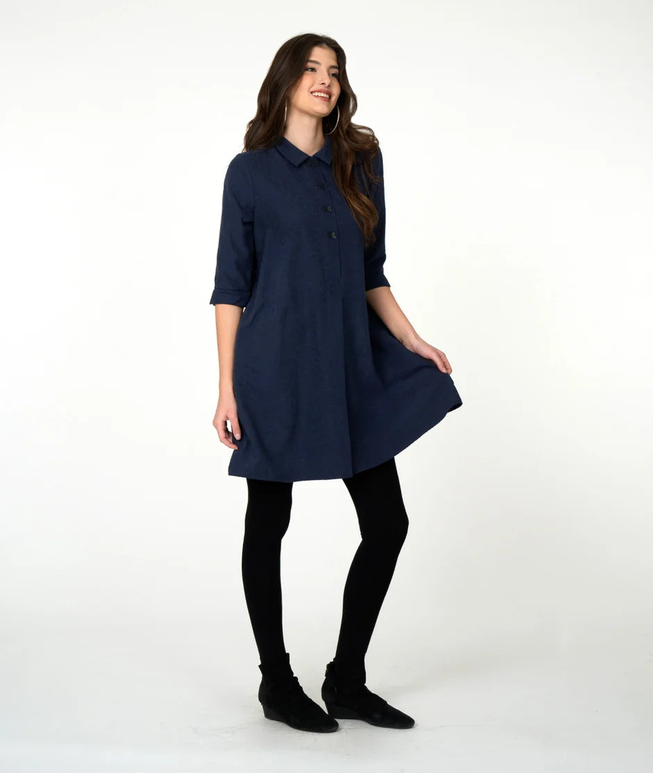 Woman wearing navy button up dress, black tights and black boots on a white background. 