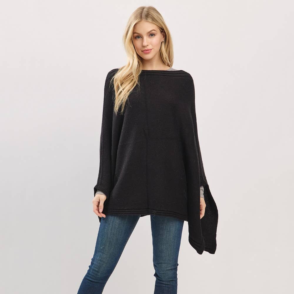 Woman wearing a black poncho over a blue top and jeans on a light gray background