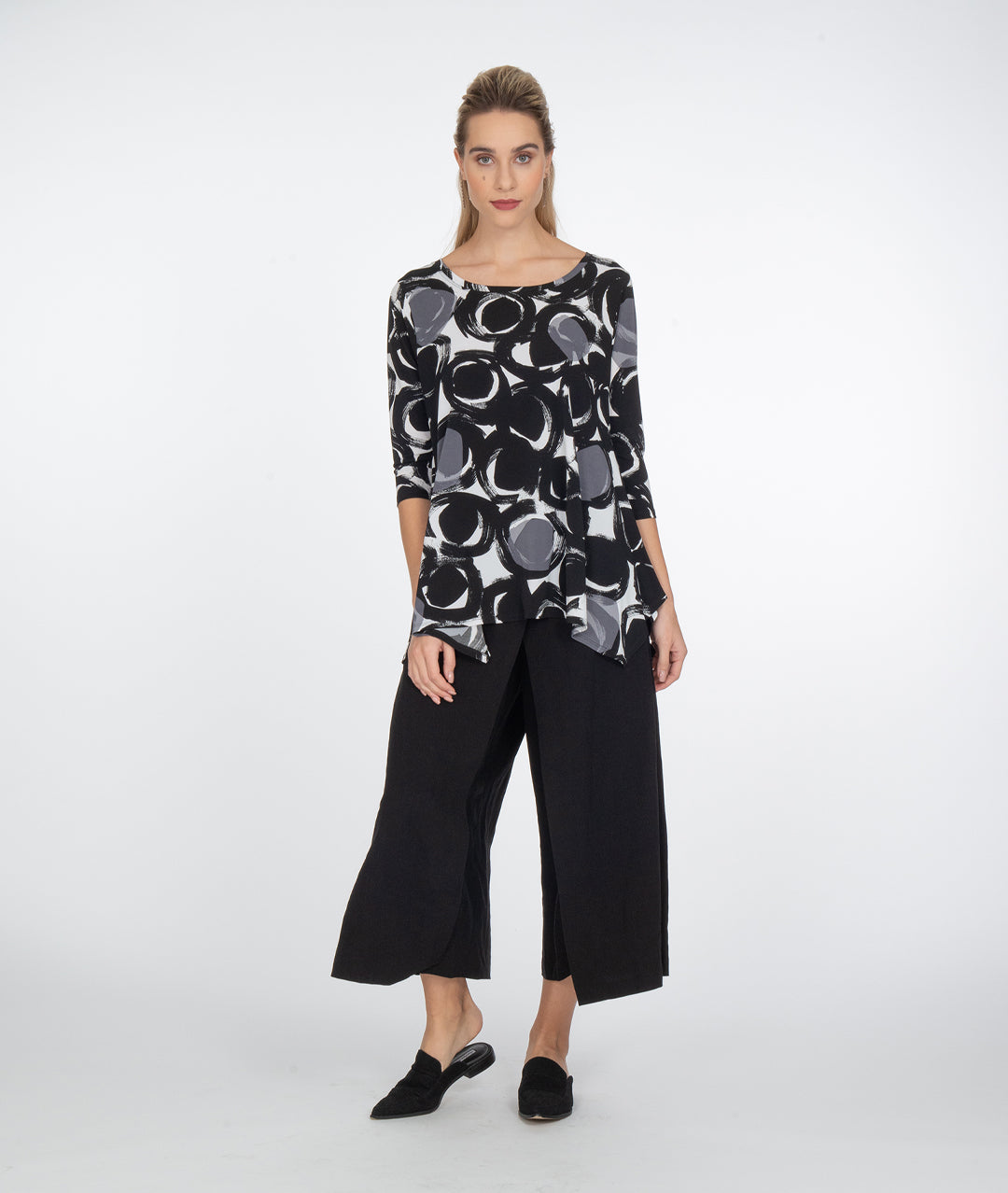 model in a wide leg black pant, with a black, white and grey circle print top with a hankerchief hem