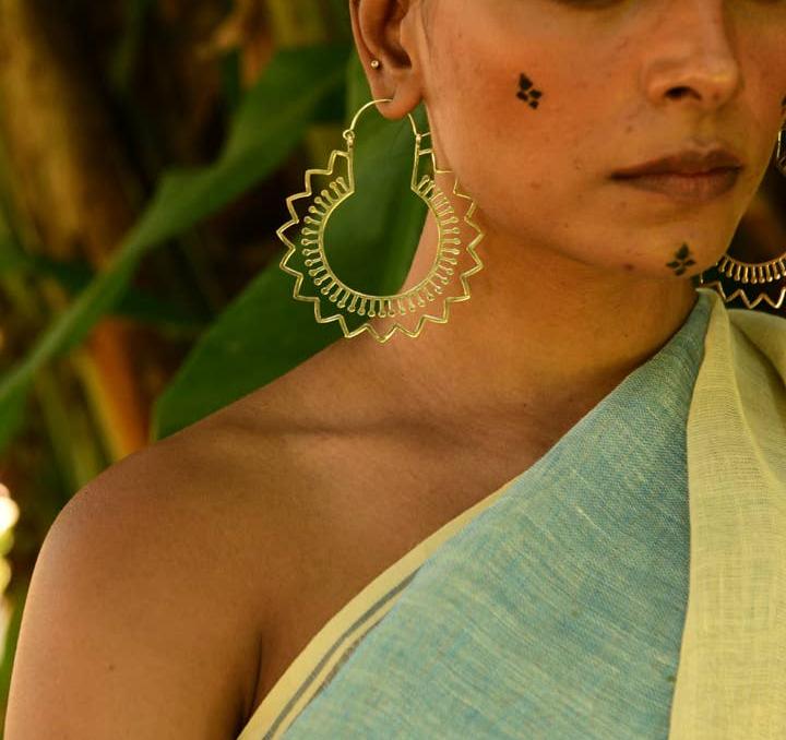 Silver plated hoop earrings with stylized flower detail shapes. on a model with green and yellow sari and greenery in the background.