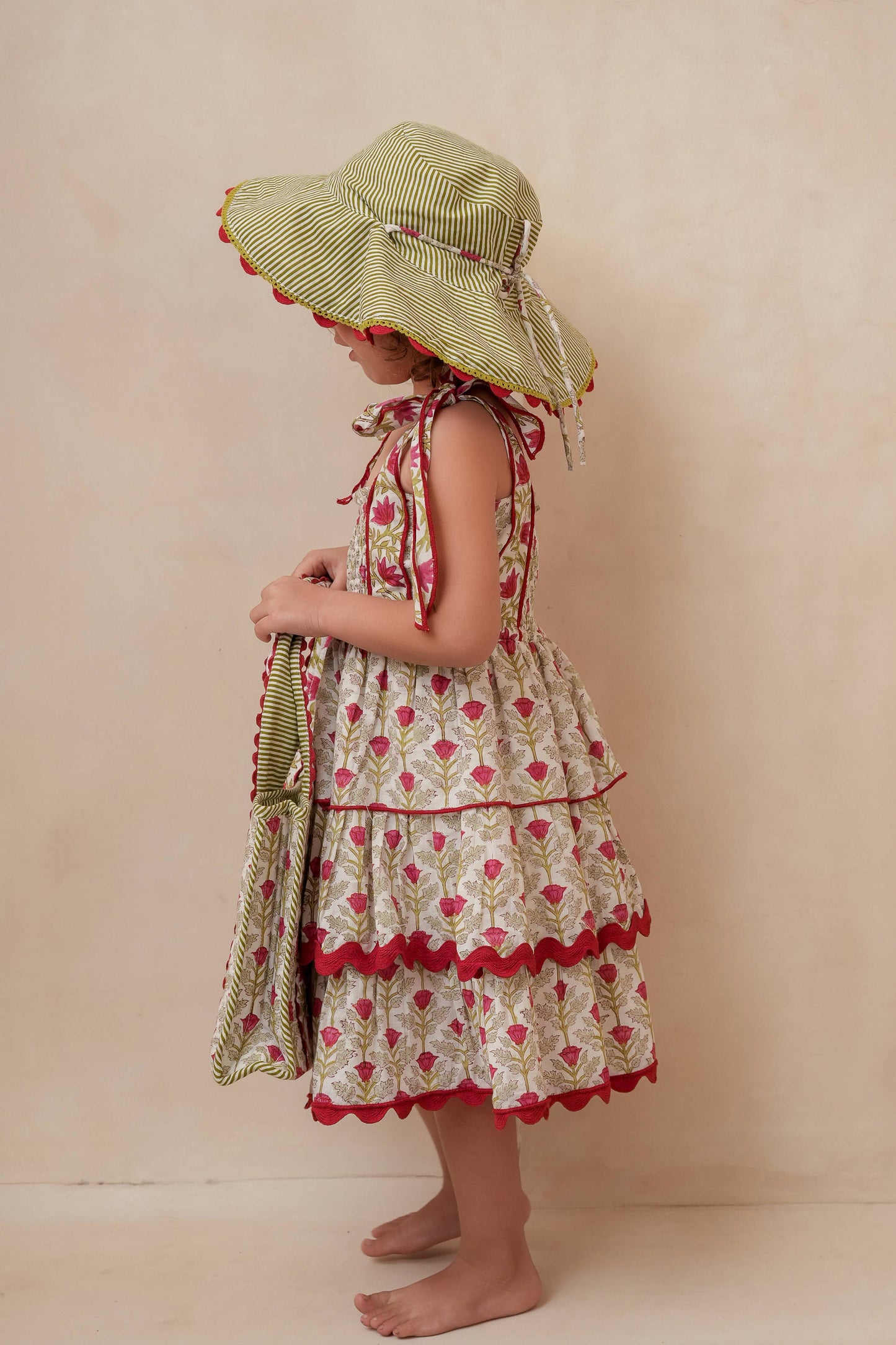 Child wearing a floral dress and sun hat against a beige background
