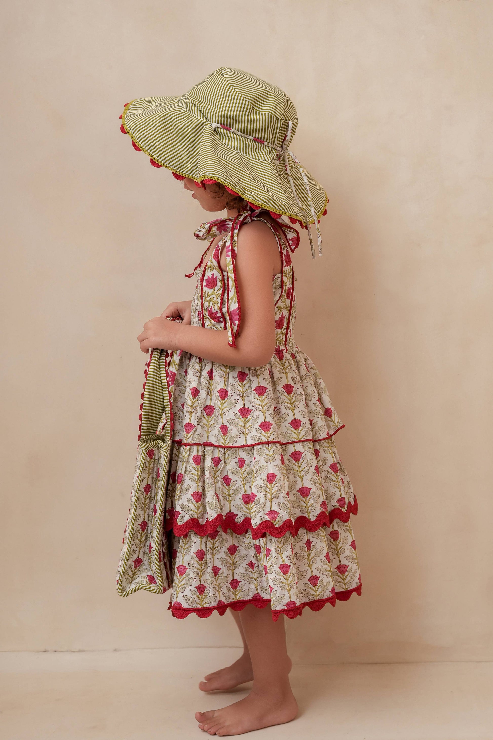 Child wearing a floral dress and sun hat against a beige background
