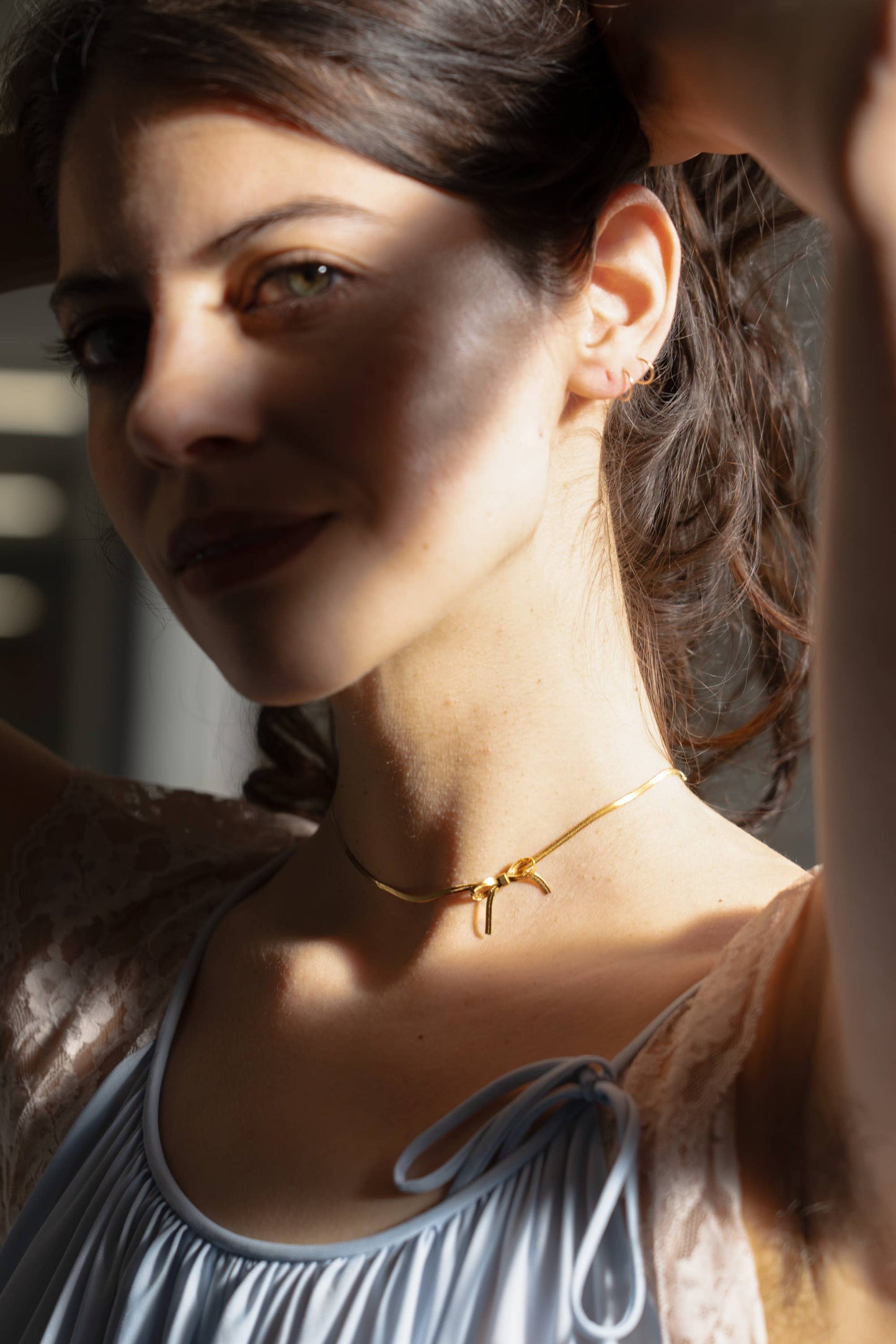 model is wearing a thin gold choker with a bow charm