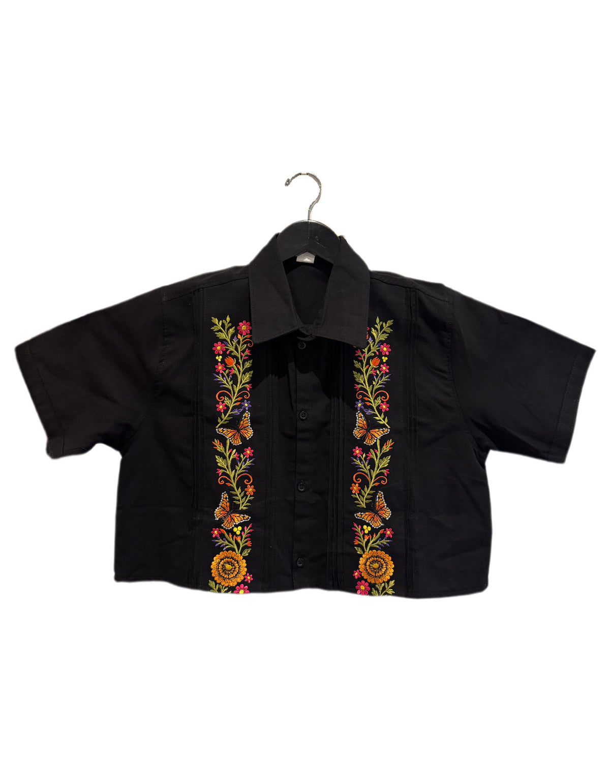 A black short-sleeve button-up shirt with colorful floral and butterfly embroidery down the front, hanging on a black hanger against a plain white background.