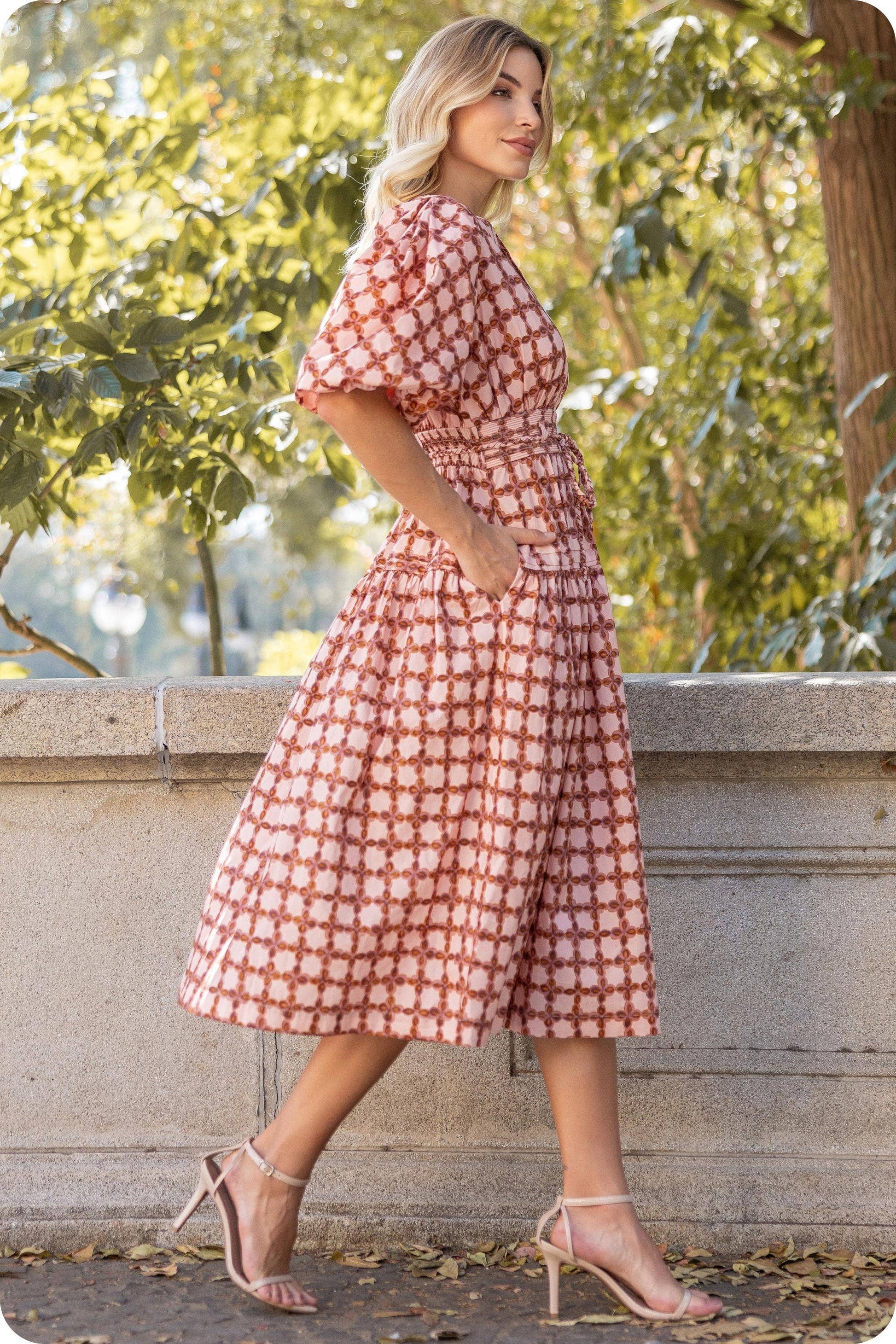 Woman wearing a red and white patterned dress standing outdoors with greenery in the background