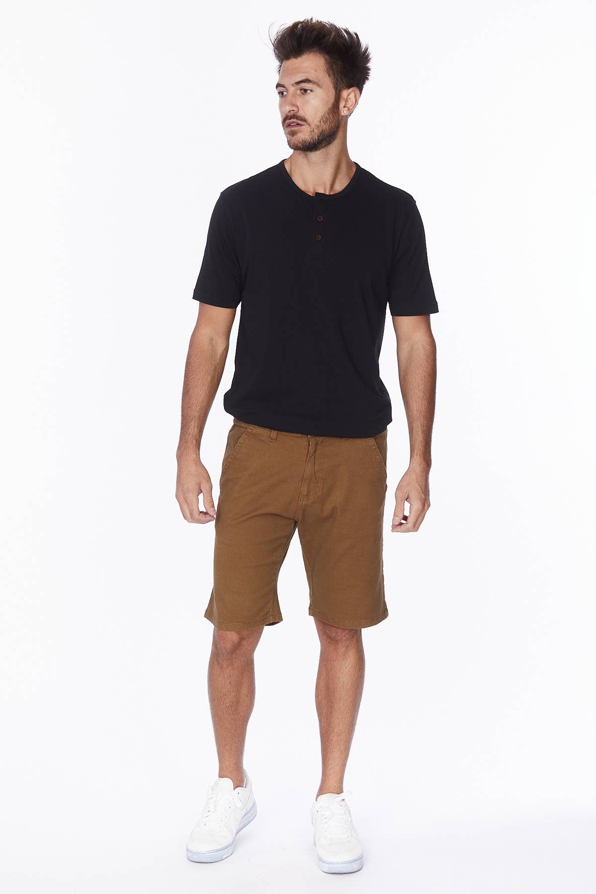 Male model wearing tobacco colored shorts with a black tee and white sneakers.