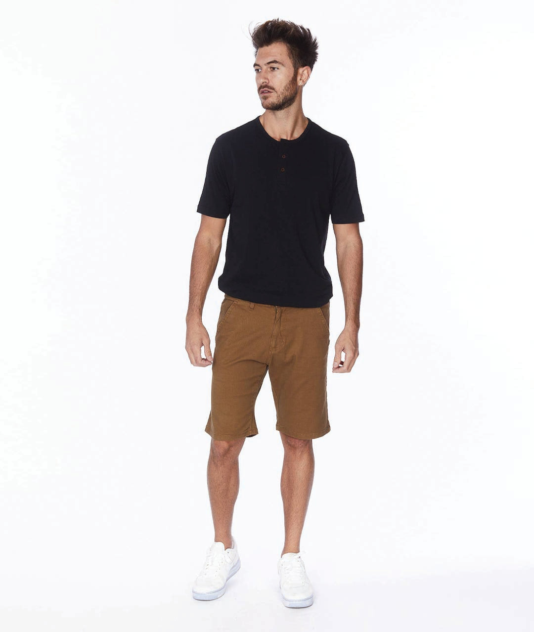 Male model wearing tobacco colored shorts with a black tee and white sneakers.