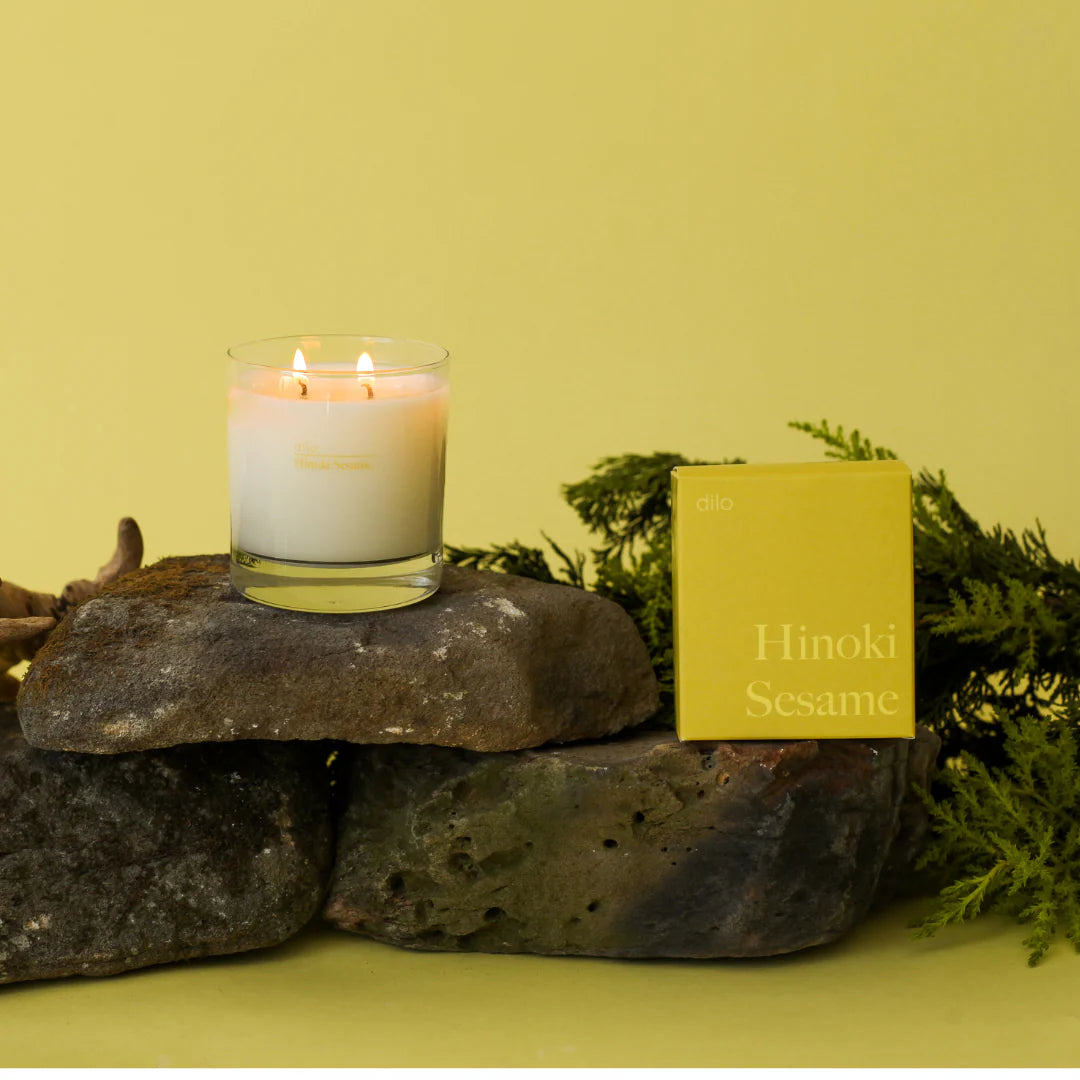 hinoki sesame scented candle with packaging on rocks and greenery