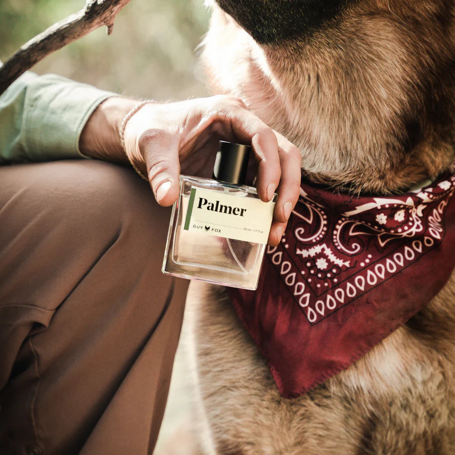 Person holding a 'Palmer' perfume bottle next to a dog wearing a bandana.