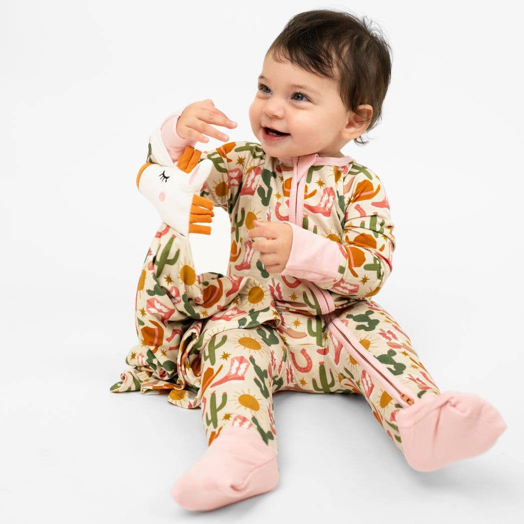 Baby wearing a colorful onesie with a pattern of animals and holding a toy on a white background