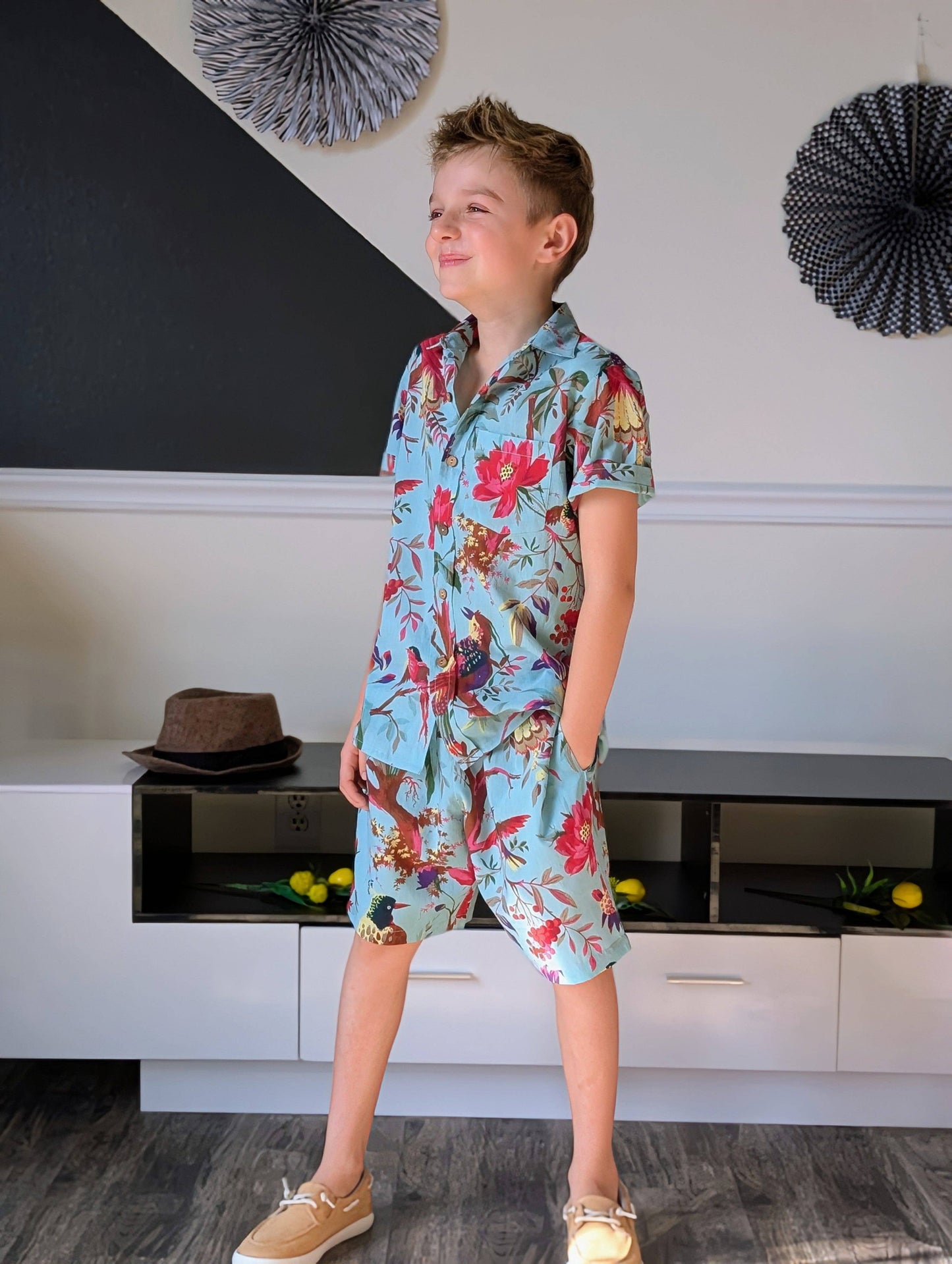 Child wearing a colorful floral shirt and shorts in a room with decorative elements.