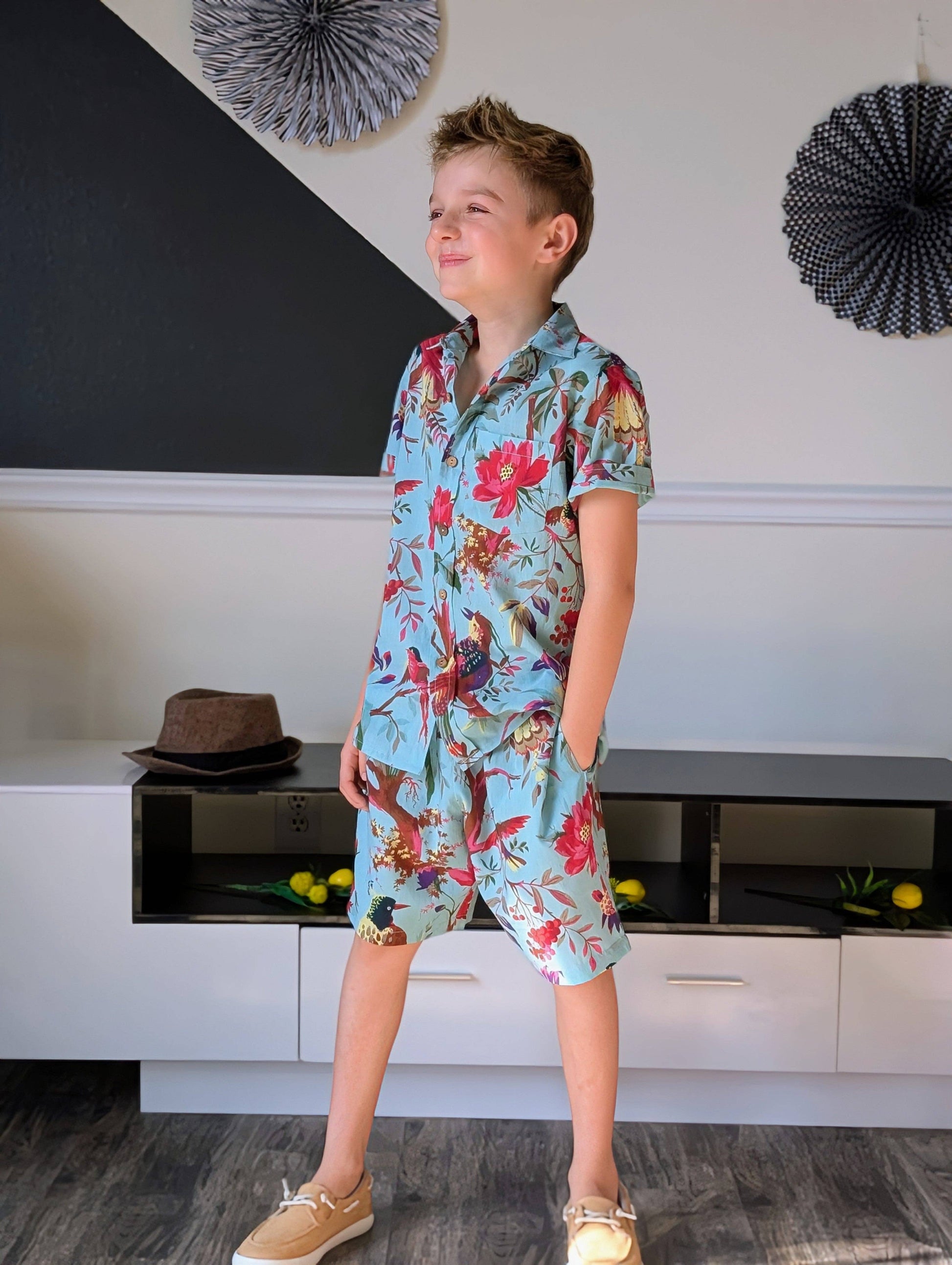 Child wearing a colorful floral shirt and shorts in a room with decorative elements.