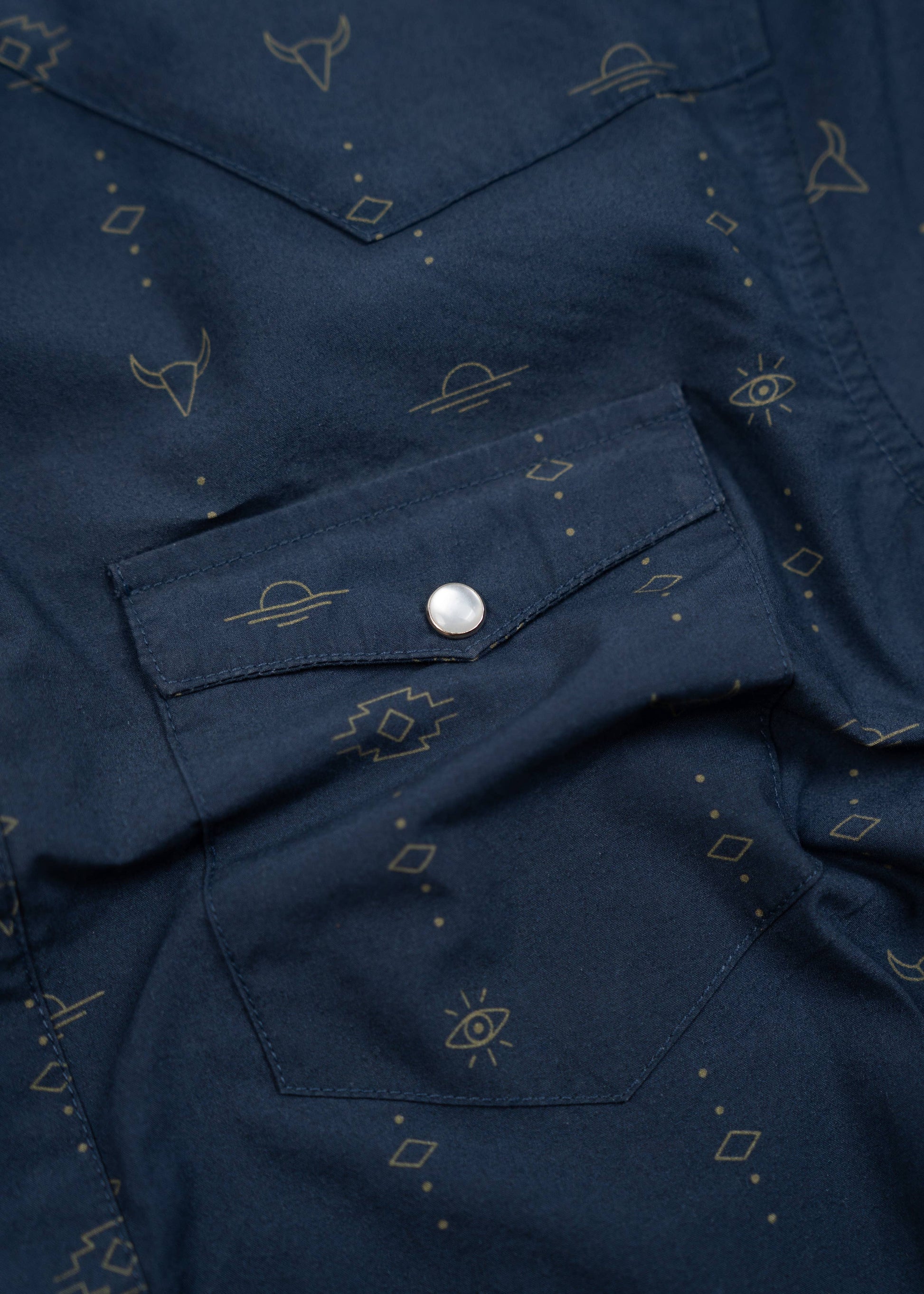 close up of chest pocket and top entry button closure with pearl snap buttons on navy western shirt with small patterns