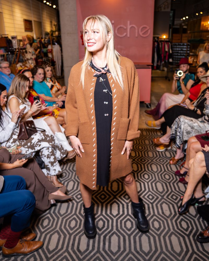 model wearing black twinbutton dress with brown cardigan, bandana and boots on a runway