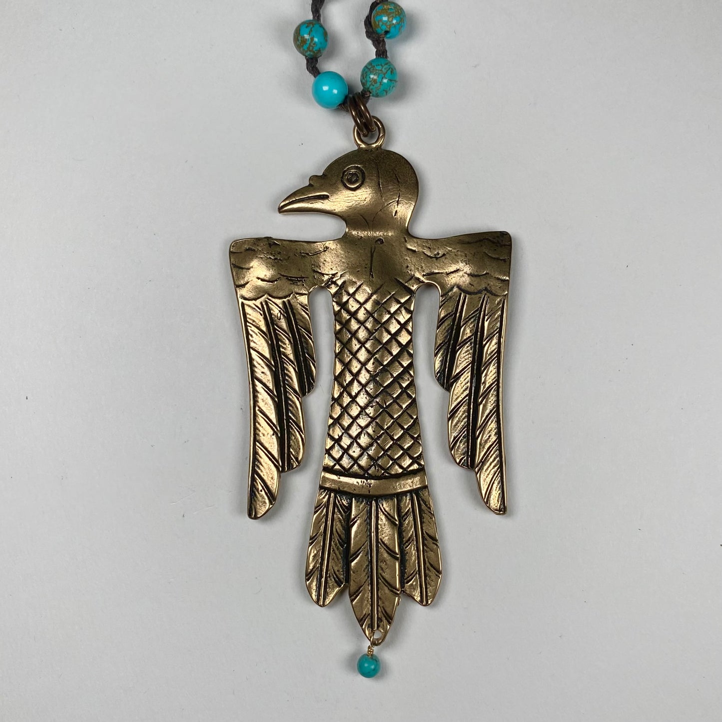 Closeup of an engraved Bronze Thunderbird pendant featuring dangling Turquoise bead.