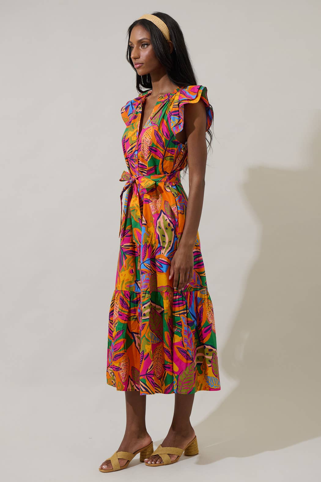 model in a midi length tropical print dress with a ruffled neckline and buttons at the center front