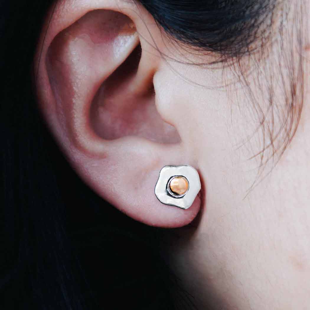 Close-up of an ear wearing a silver earring with a peach-colored gemstone.
