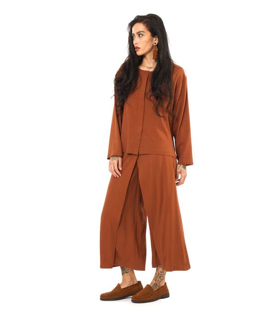 model in a rust color wide leg pant with an overlay in the front, with a matching long sleeve top with a false placket 