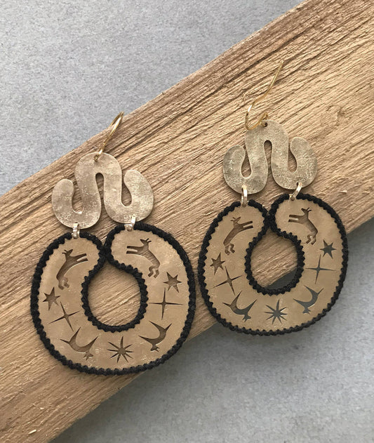 Pair of earrings with intricate designs on a wooden and gray surface