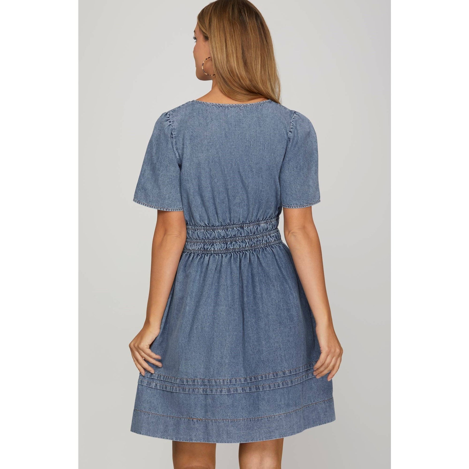 A woman showing back of blue washed denim short sleeve dress with elastic waistband 