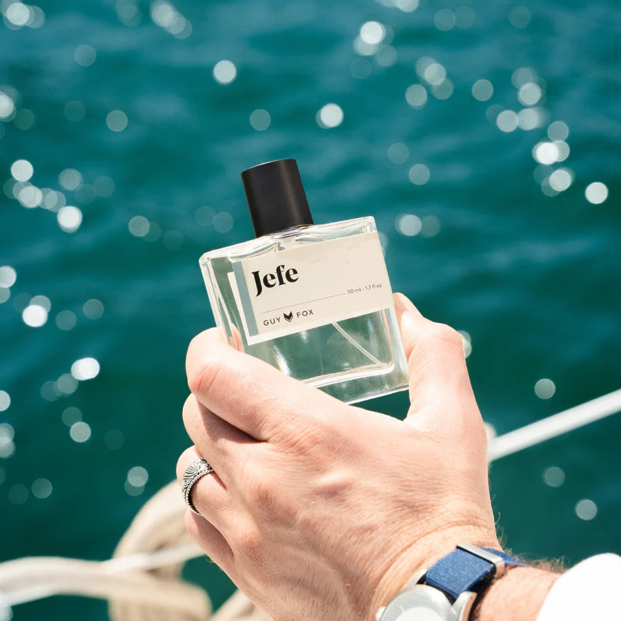 Hand holding a bottle of Jefc perfume with a blurred blue water background