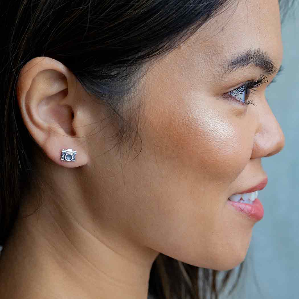 Close-up of a woman wearing a camera-shaped earring with a blurred background