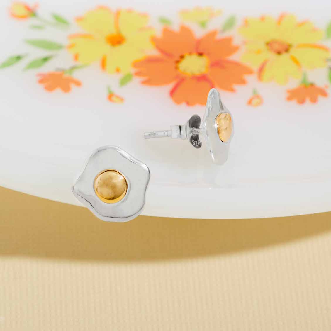 Silver and gold stud egg earrings on a floral background